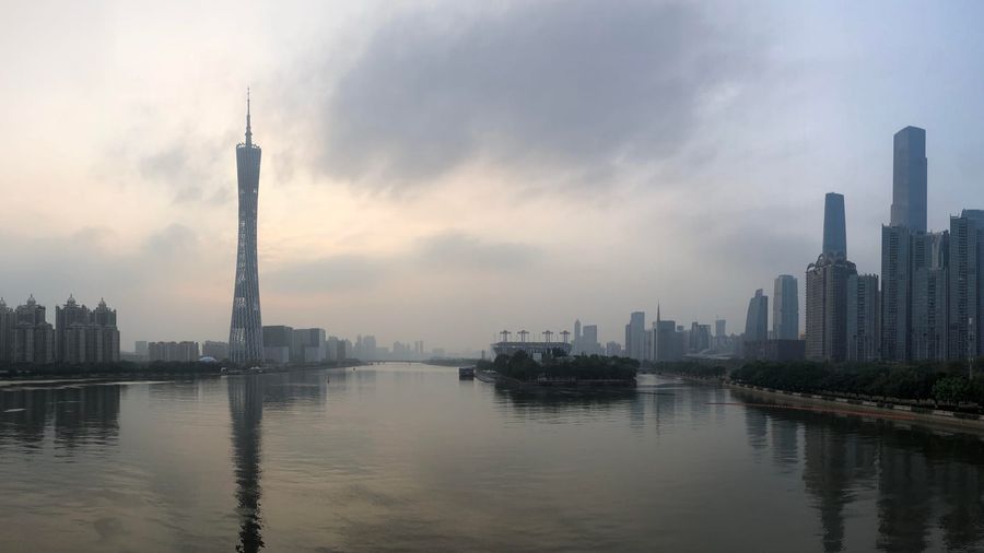 The Guangzhou skyline split by the Pearl River, with the Tianhe CBD towers on one bank and the slender Canton Tower rising on the opposite side under a hazy sky