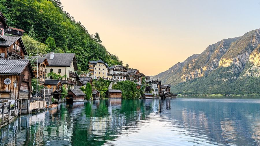 Wooden lakeside houses of Hallstatt reflected in the calm Hallstätter See at sunset, the Dachstein mountains rising beyond