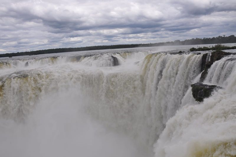 The Devil's Throat at Iguazú Falls in full flow, with spray rising from the gorge under a cloudy sky on the Argentine side