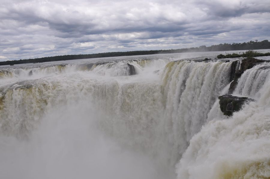 The Devil's Throat at Iguazú Falls in full flow, with spray rising from the gorge under a cloudy sky on the Argentine side