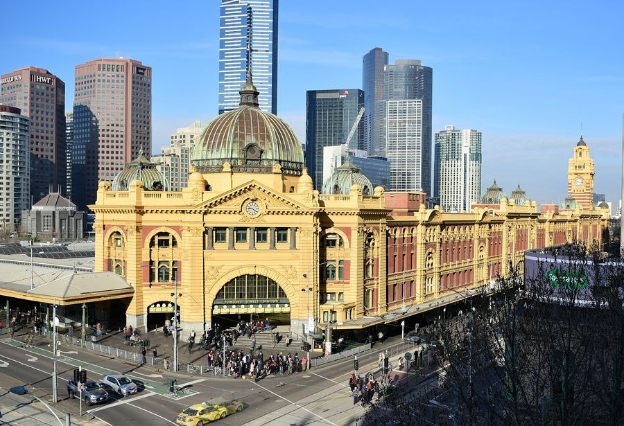 The yellow Edwardian facade and green copper dome of Flinders Street Station in central Melbourne, with trams and pedestrians