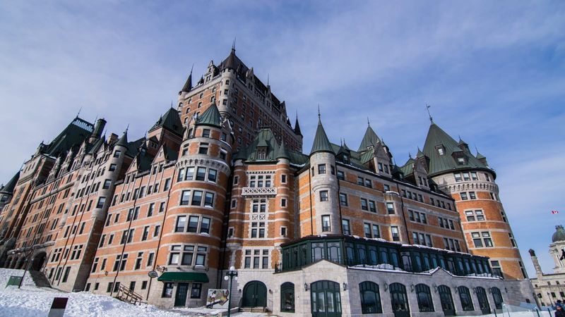 The Château Frontenac hotel rising above the snow-covered rooftops of Old Quebec on a clear winter day, with the frozen St. Lawrence River beyond