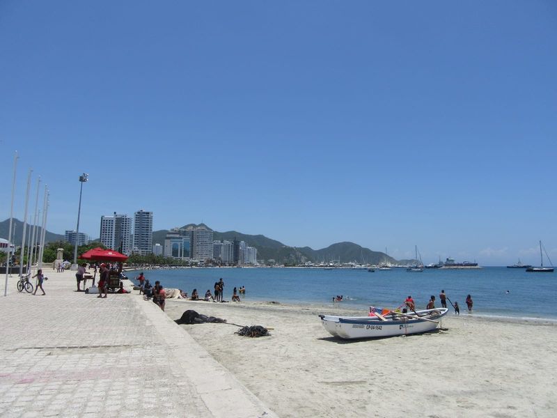 The Bay of Santa Marta seen from the northern end of the Camellón Rodrigo de Bastidas waterfront, with fishing boats on calm water and the Sierra Nevada foothills rising behind the city