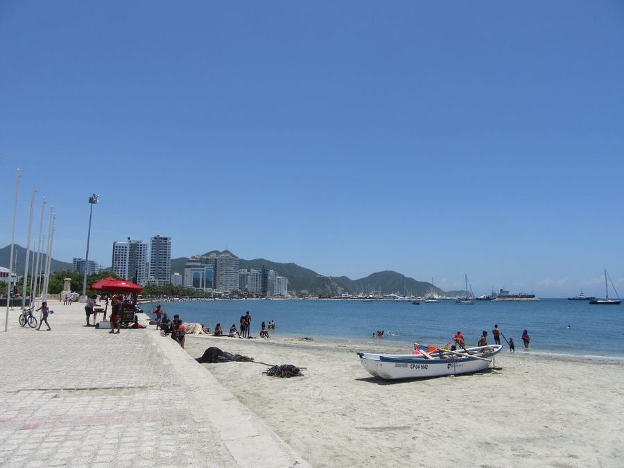 The Bay of Santa Marta seen from the northern end of the Camellón Rodrigo de Bastidas waterfront, with fishing boats on calm water and the Sierra Nevada foothills rising behind the city