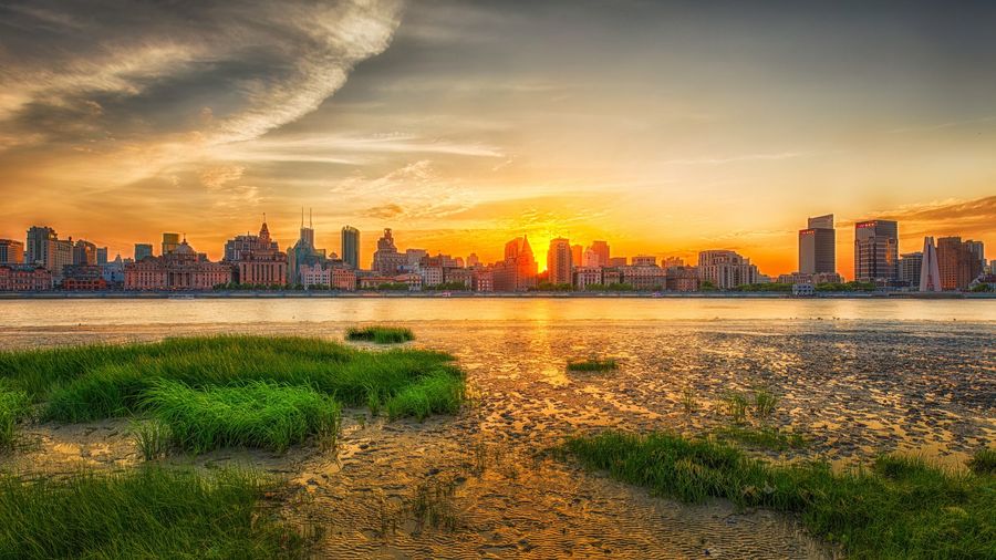 The historic Bund waterfront in Shanghai at sunset, with the illuminated glass towers of the Pudong skyline rising across the Huangpu River