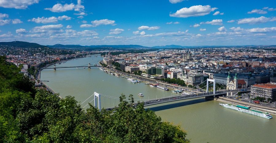 An elevated view over Budapest and the Danube from Gellert Hill, with the white Elisabeth Bridge and the Chain Bridge spanning the river and cruise boats moored along the banks