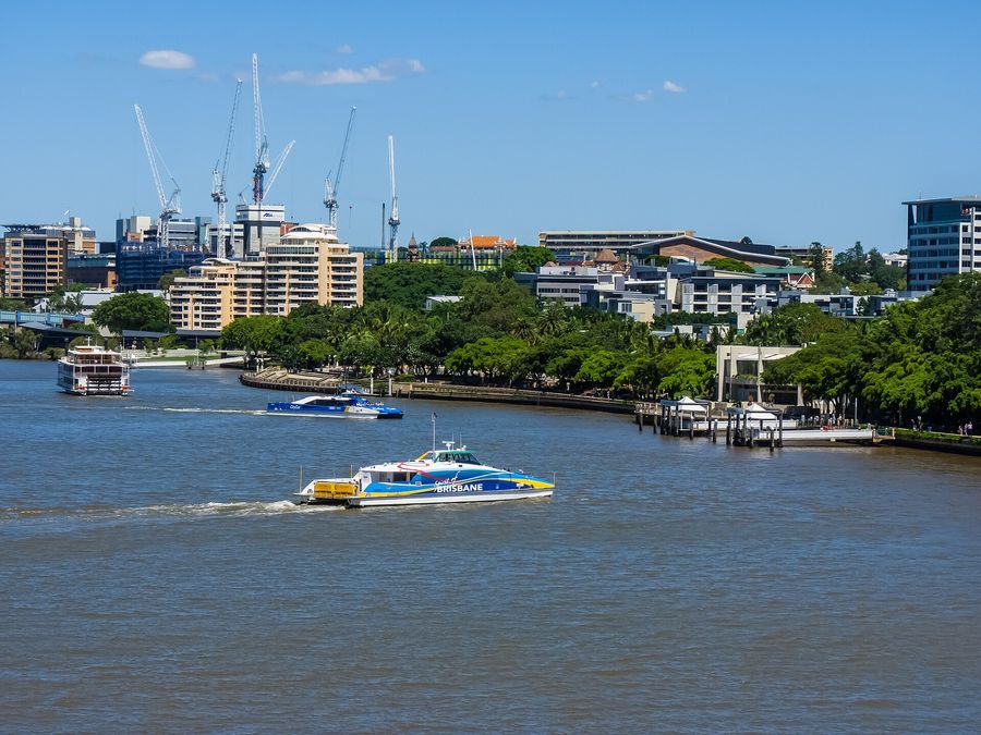 A blue-and-white CityCat catamaran ferry approaching the South Bank terminal on the Brisbane River, another CityCat behind it