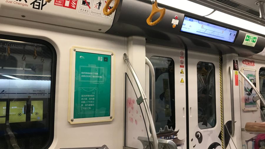 Interior of a panda-decorated Chengdu Metro Line 10 train with yellow hand straps, a digital route display, and "Just Chengdu" branding above the doors