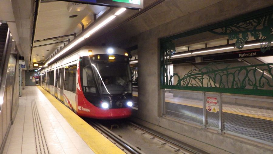 A red-and-white OC Transpo O-Train light-rail vehicle approaching the underground platform at Parliament (Parlement) Station on Ottawa's Confederation Line