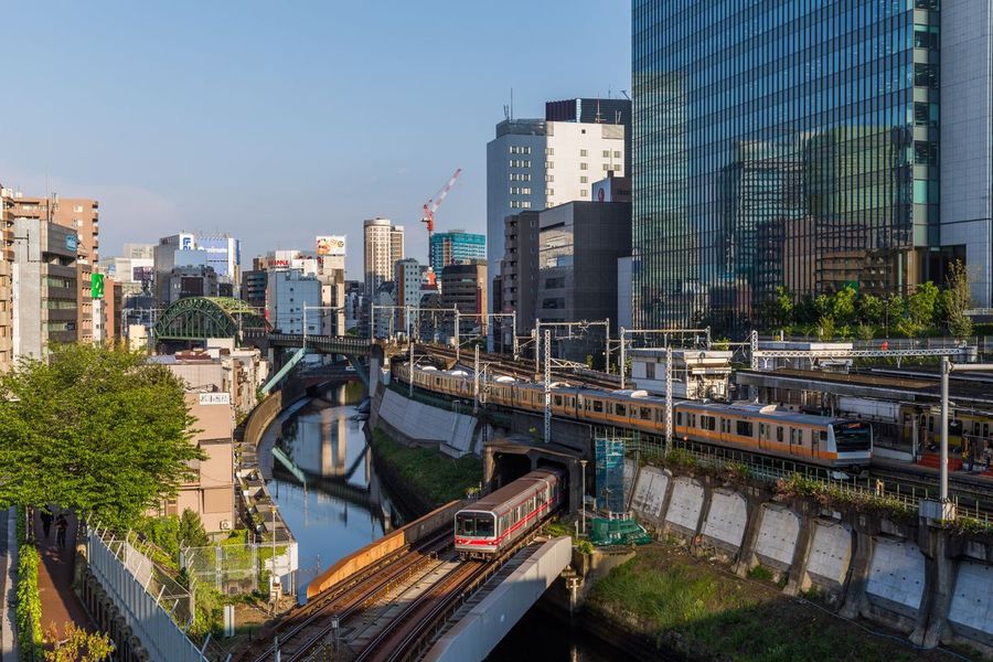 Orange-striped JR commuter trains and a red Marunouchi-line subway train crossing the Kanda River among the high-rise buildings of Ochanomizu in Tokyo