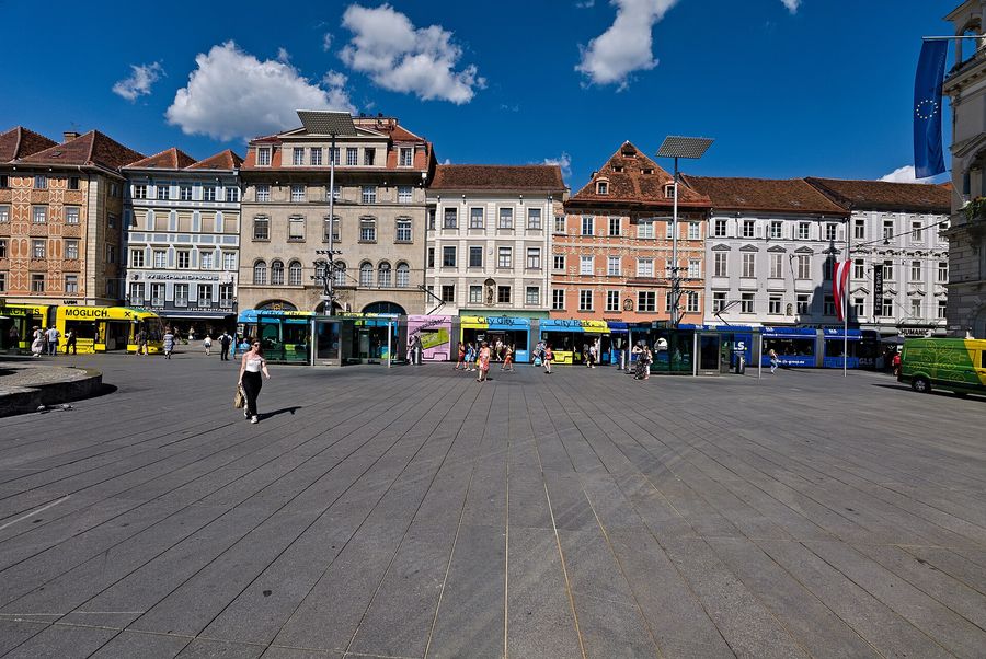 Hauptplatz, the main square of Graz, Austria, lined with pastel historic facades and crossed by trams on a clear summer day