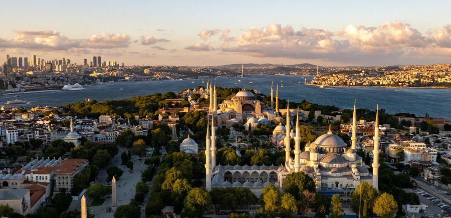 A golden-hour aerial view of Istanbul's historic peninsula with Hagia Sophia and the minarets of the Blue Mosque, the Bosphorus and its suspension bridge in the background