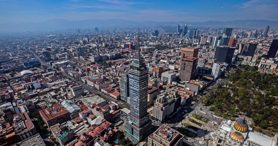 An aerial view of Mexico City's historic centre with the Torre Latinoamericana skyscraper rising above the sprawl, the domed Palacio de Bellas Artes and mountains on the horizon