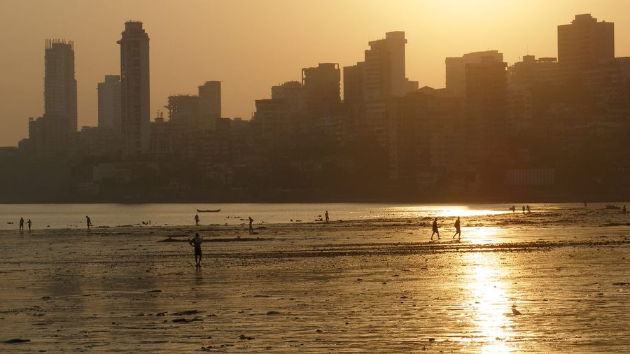 Mumbai's high-rise skyline glowing at sunset above Girgaon Chowpatty beach and the curve of Marine Drive