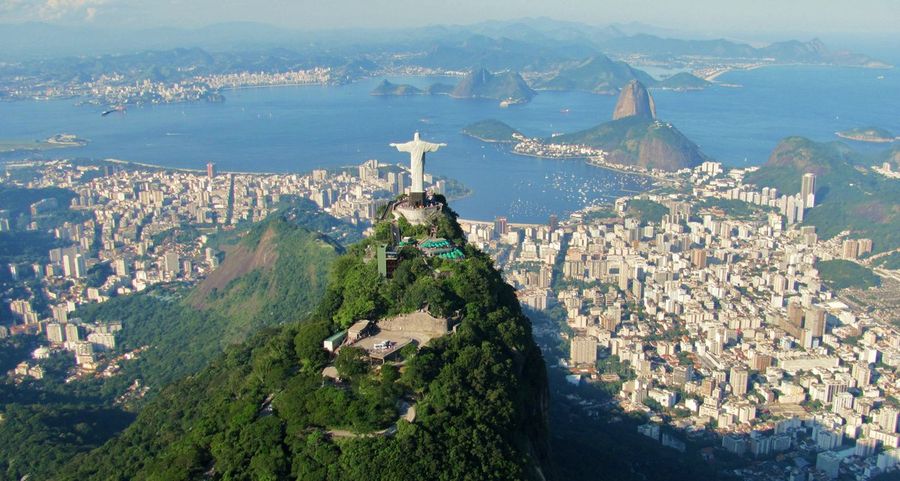 An aerial view of Rio de Janeiro with the Christ the Redeemer statue atop forested Corcovado mountain, Sugarloaf Mountain and Guanabara Bay beyond the city