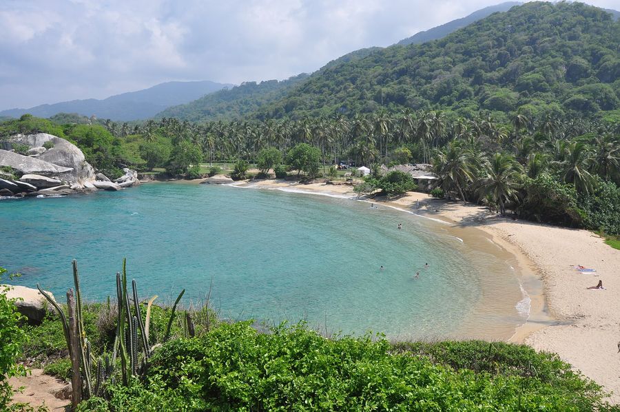 The thatched lookout hut on the rocky headland at Cabo San Juan del Guía in Tayrona National Park near Santa Marta, framed by two turquoise Caribbean coves and jungle-covered hills