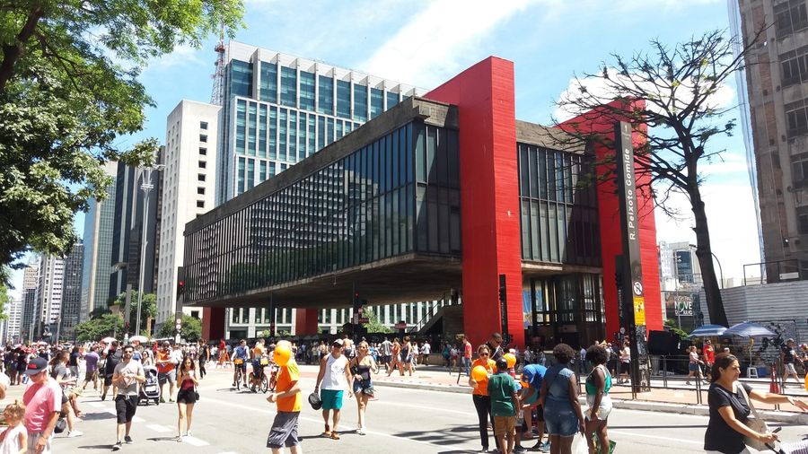 Crowds of pedestrians and cyclists on a car-free Avenida Paulista on a Sunday in São Paulo, beneath the red beams and suspended glass hall of the MASP art museum