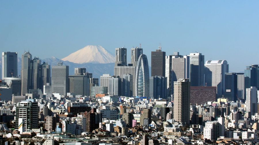 The dense high-rise skyline of Tokyo's Shinjuku district with the snow-capped cone of Mount Fuji visible on the horizon under a clear blue sky