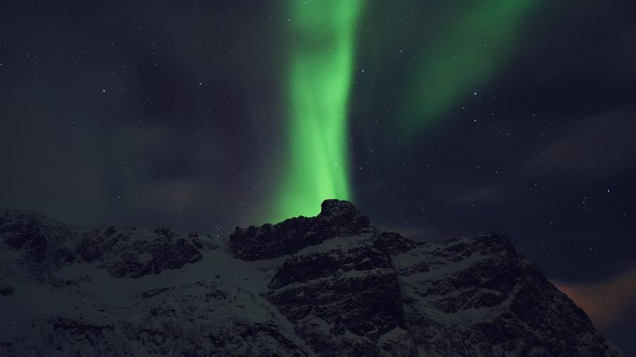 Green aurora borealis rippling across the night sky above a snowy landscape near Tromso in northern Norway