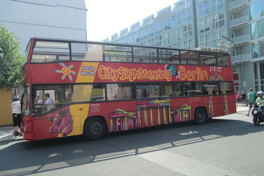 A red open-top double-decker City Sightseeing hop-on hop-off tour bus parked on a Berlin street as passengers board